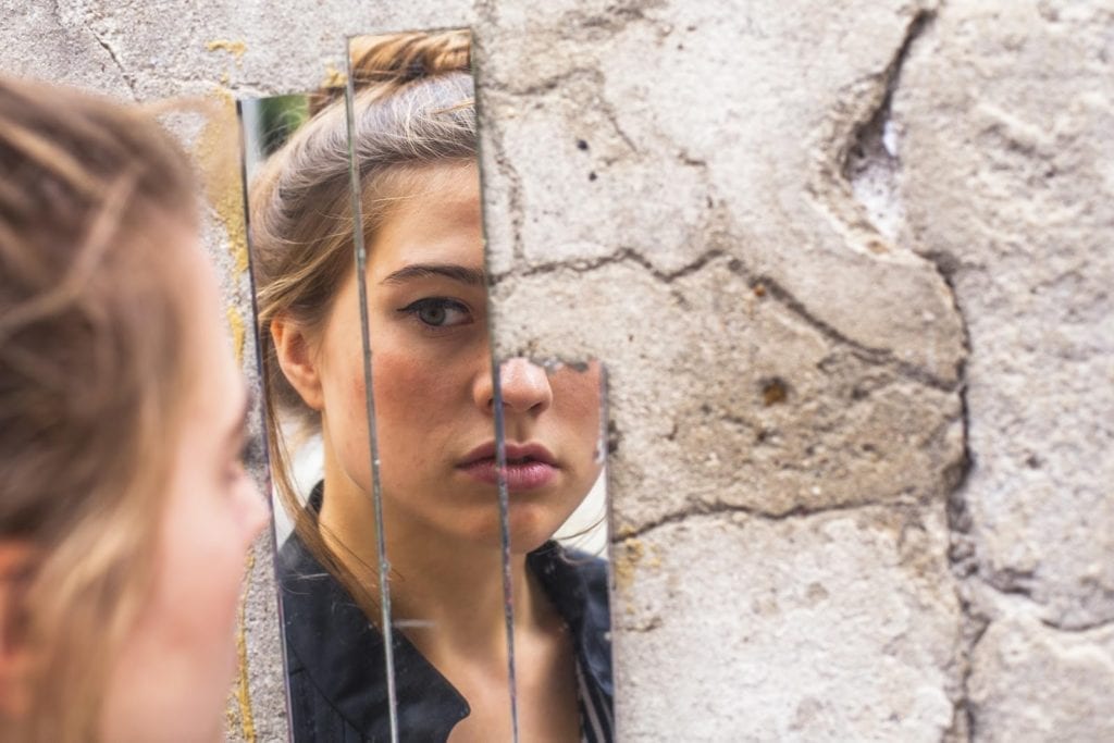 Woman looking at her reflection in a cracked mirror