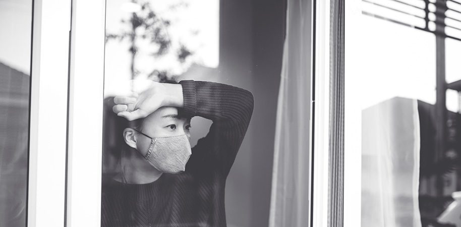 Woman wearing a medical mask looking out the window