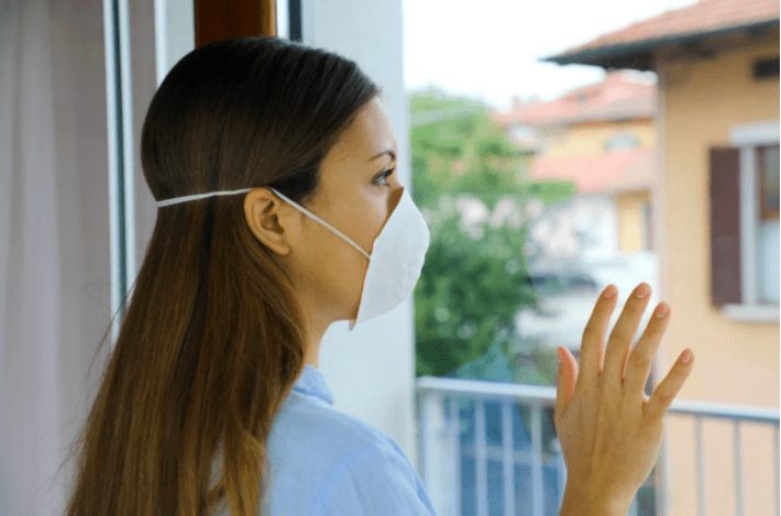 Woman wearing a protective mask looking out the window