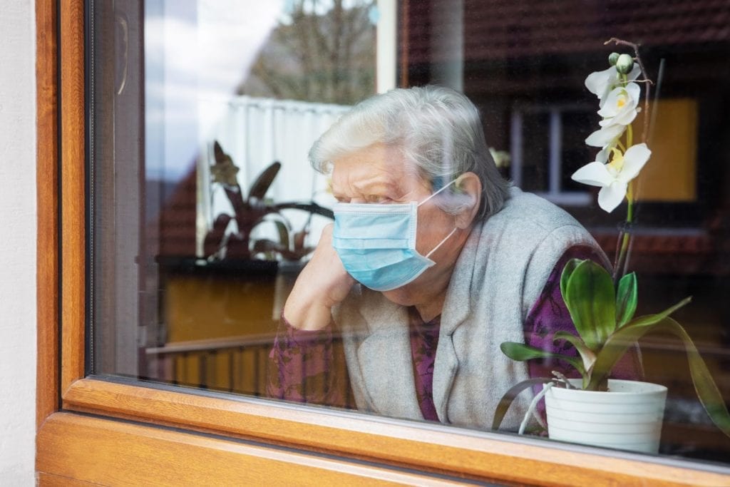 Elderly female wearing a protective mask looking out of the window