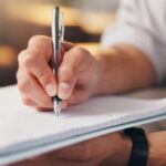 Close-up of a person writing notes on a clipboard, with the BrainsWay logo.